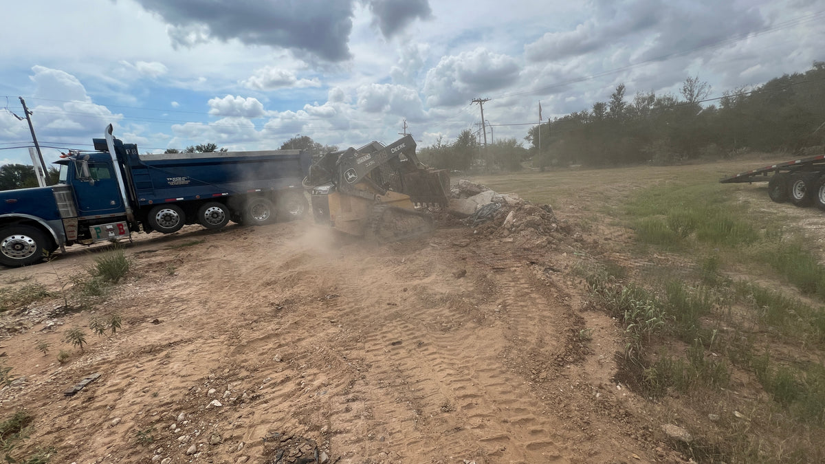 Skid steer loading concrete debris into an 18-ton tri-axle dump truck for haul-off in Austin, Texas.